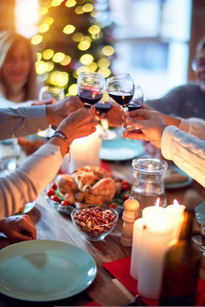 Des personnes trinquent avec leurs verres de vin au dessus d’une table garnie d’un repas