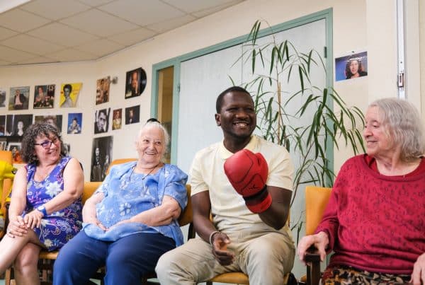 Deux collaborateurs d’entreprise et deux personnes âgées bénéficiaires du centre d’accueil Delta7 rient aux éclats lors d’un team building d’improvisation théâtrale organisé par Lutila.