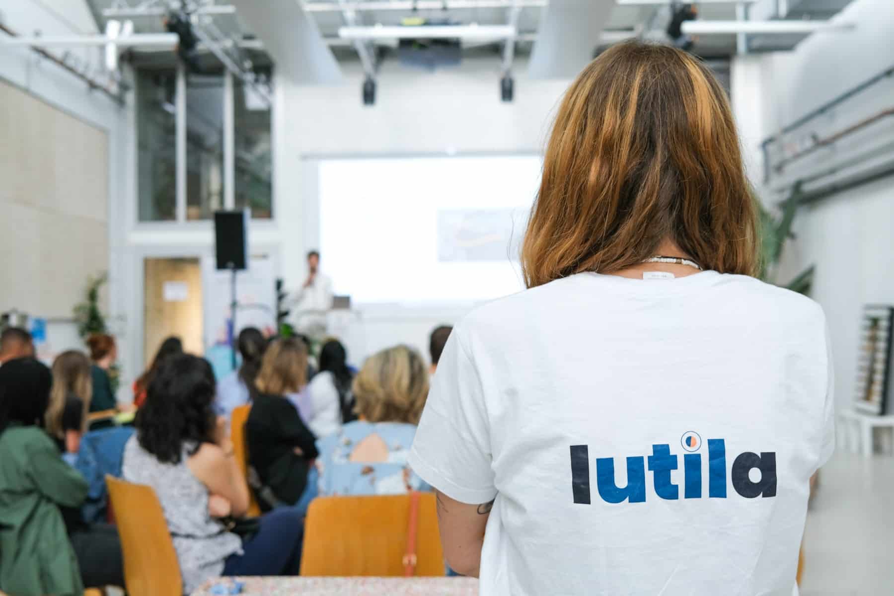 Des collaborateurs d'entreprise assistent à une table ronde organisée par Lutila, dans le cadre d'un team building solidaire. Au premier plan, une experte en événementiel solidaire porte un t-shirt avec le logo de Lutila.