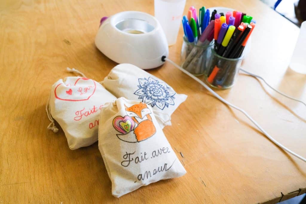 Trois petits sacs en tissu décorés sont posés sur une table. Ils contiennent des kits de soin à destination de publics précaires, réalisés par des collaborateurs d’entreprise dans le cadre d’un team building solidaire organisé par Lutila.