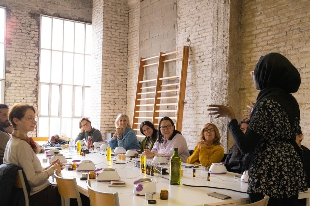 Des collaborateurs d’entreprise réunis autour d’une table écoutent attentivement une animatrice, dans le cadre d’un team building DIY de fabrication de produits cosmétiques à destination de publics précaires, organisé par Lutila.